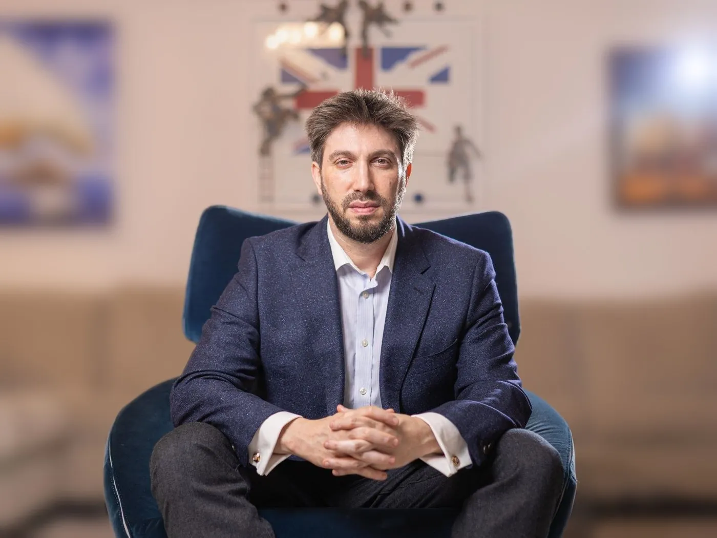 Daniel Seal seated in a blue armchair in his London office, a Union Jack artwork behind him